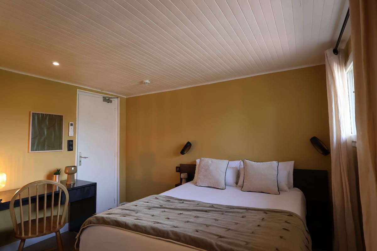 A hotel room with a bed, desk, chair, and a door.