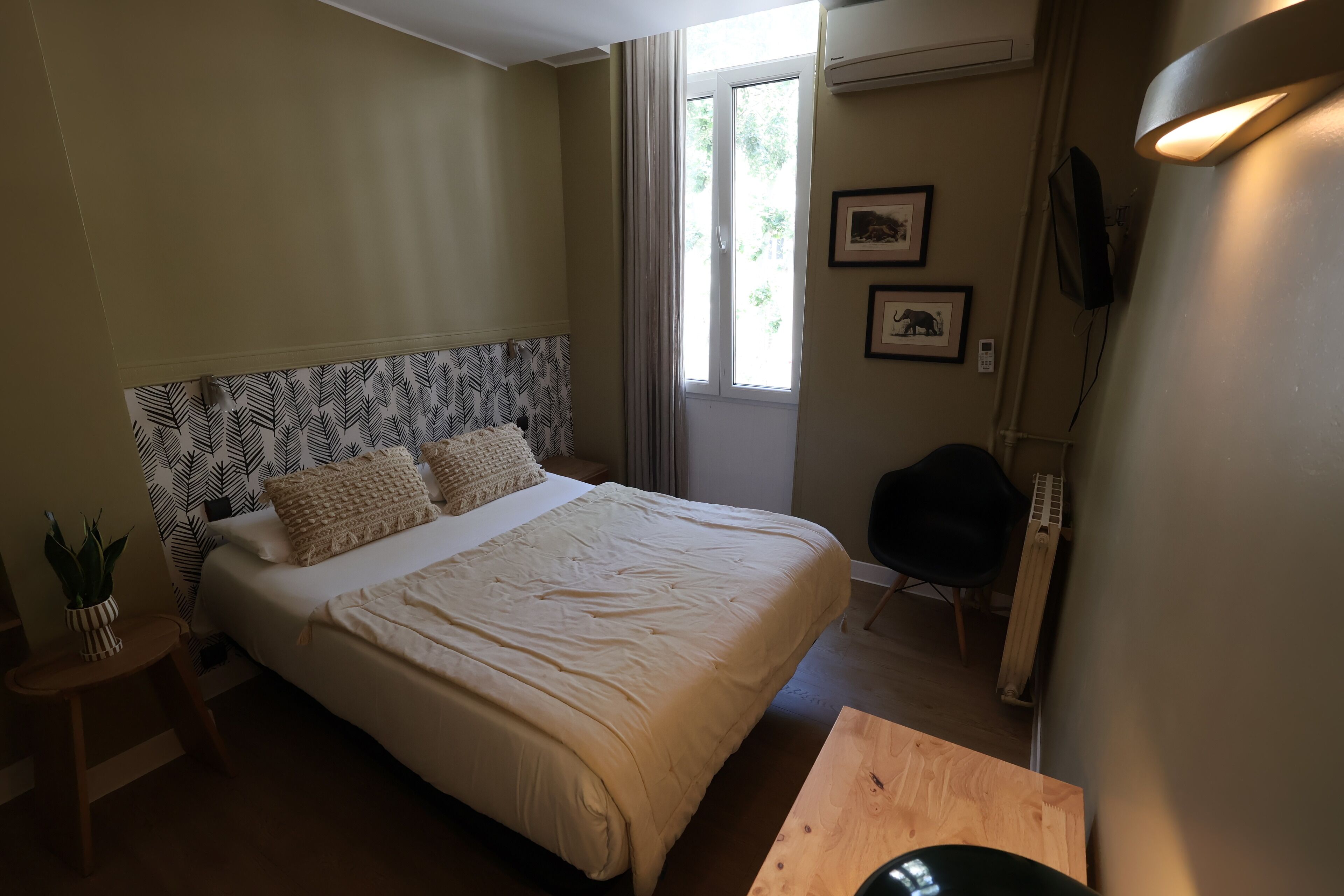 Un dormitorio con cama, una silla, una mesa, una planta en maceta y un ventanal con cortinas.