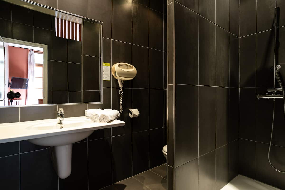 A modern bathroom with a white sink, a mirror, a hairdryer, and a shower.