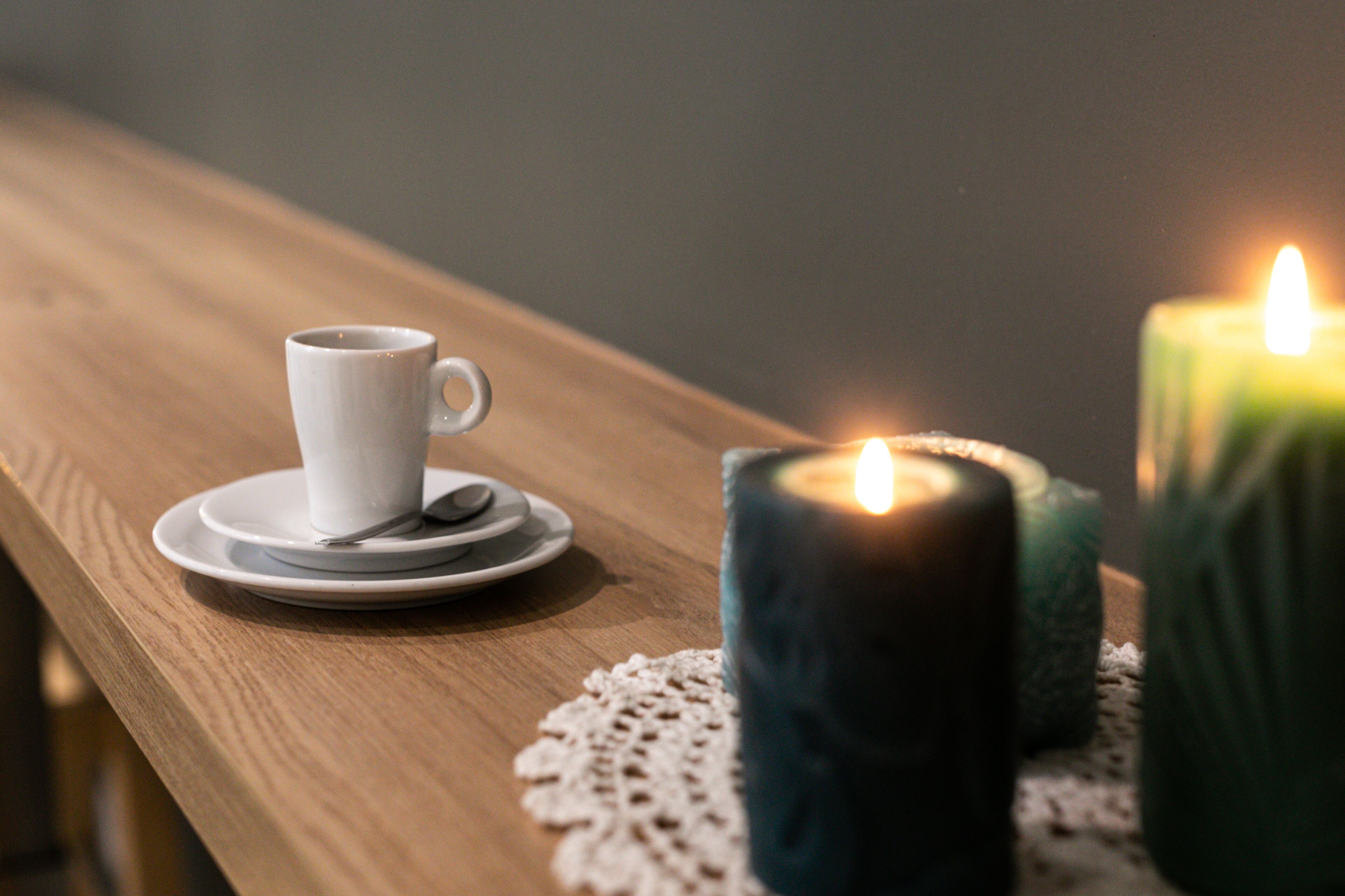A wooden table with a white cup and saucer, a candle, and a doily.