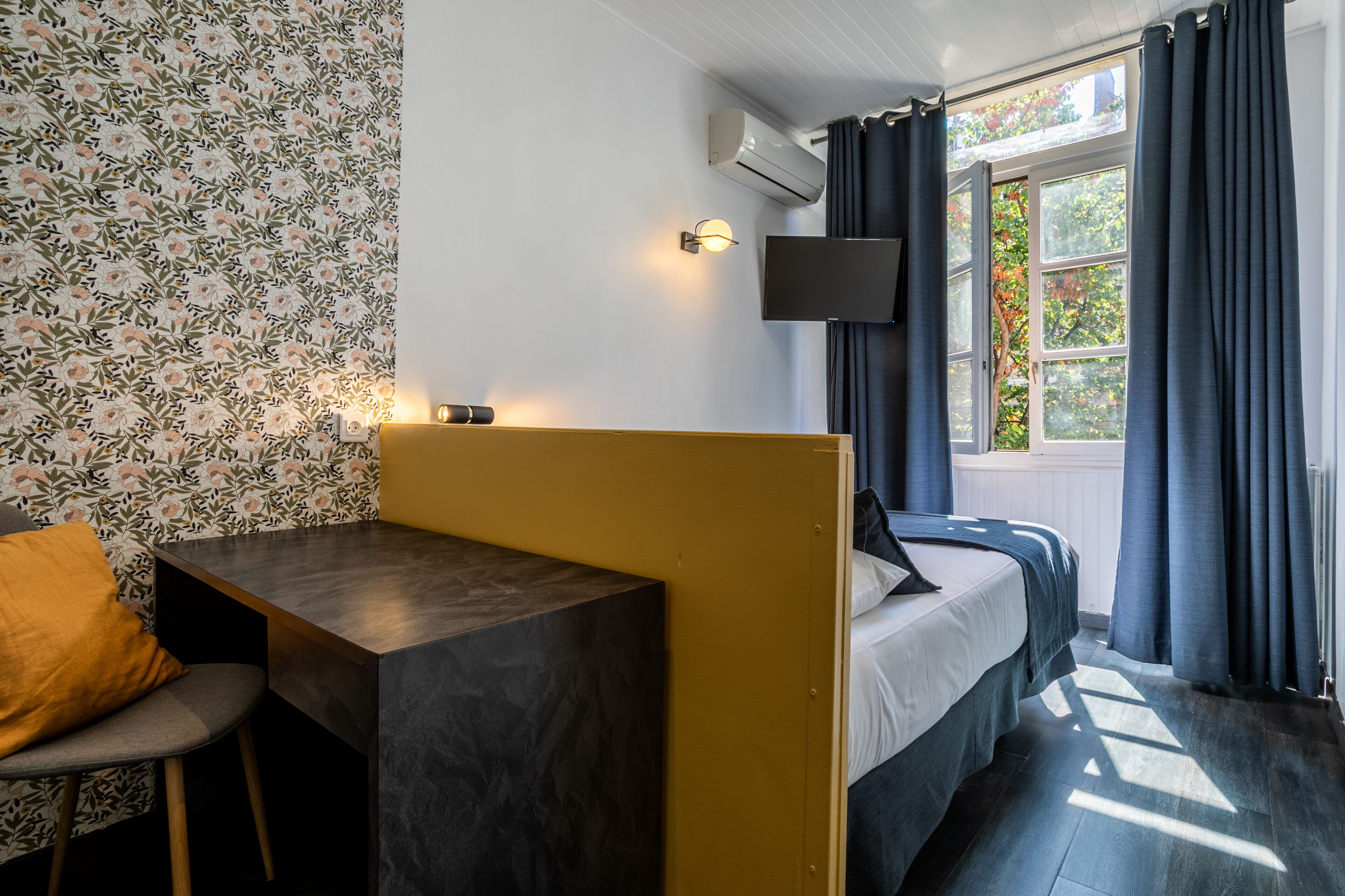 Une chambre avec un lit, un bureau, une chaise, une télévision et une fenêtre avec des rideaux.