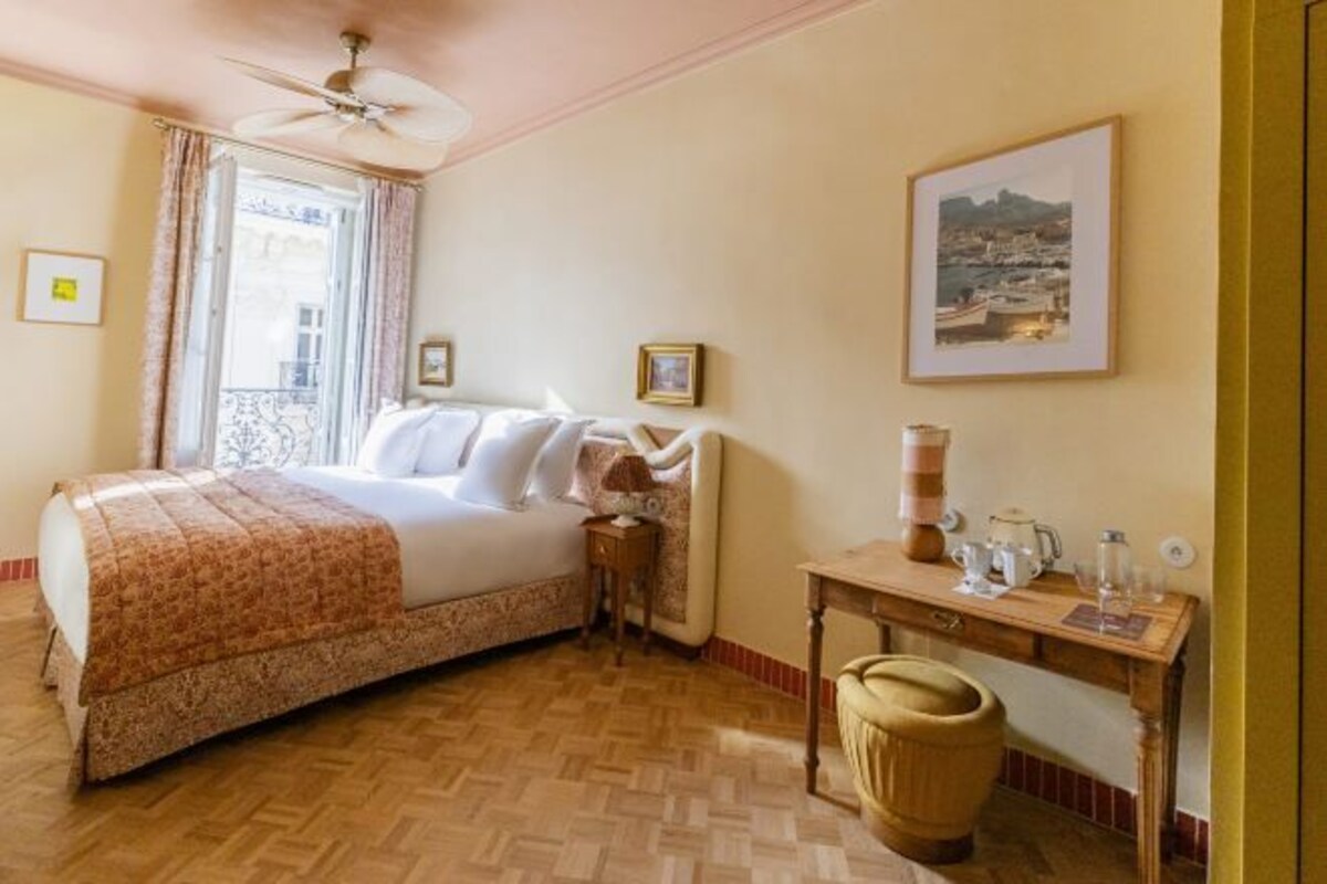 Habitación de hotel con cama, escritorio, silla, ventilador de techo y ventana con cortinas.