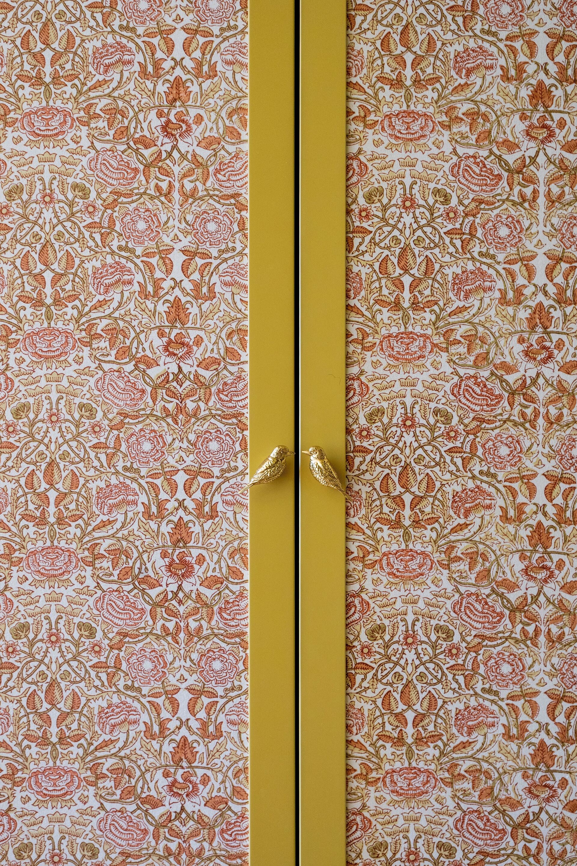 Un armario con estampado floral y dos pomos dorados con forma de pájaro.