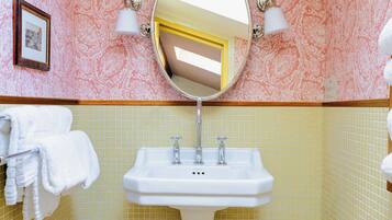 A bathroom with a pedestal sink, two wall-mounted lights, a mirror, and patterned wallpaper.