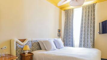 A bedroom with a bed, a ceiling fan, a nightstand, a lamp, and a window with curtains.