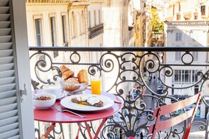 Un balcon avec une table préparée pour le petit-déjeuner, comprenant des croissants, un verre de jus d’orange et une assiette avec un œuf poché.