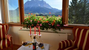 A room with a table set for two, a window with a view of mountains, and a potted plant with flowers. - Sporthotel Zugspitze (Lermoos)