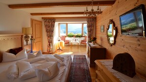 A wooden-paneled bedroom with a large bed, a chandelier, a view of the outdoors, and a mirror on the wall. - Sporthotel Zugspitze (Lermoos)