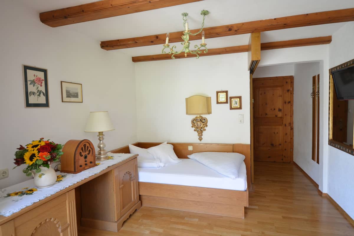 A bedroom with a wooden bed, a nightstand with a lamp, a dresser, and a wall-mounted TV.