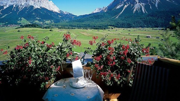 A table set outdoors with a mountain view, surrounded by greenery and flowers. - Sporthotel Zugspitze (Lermoos)