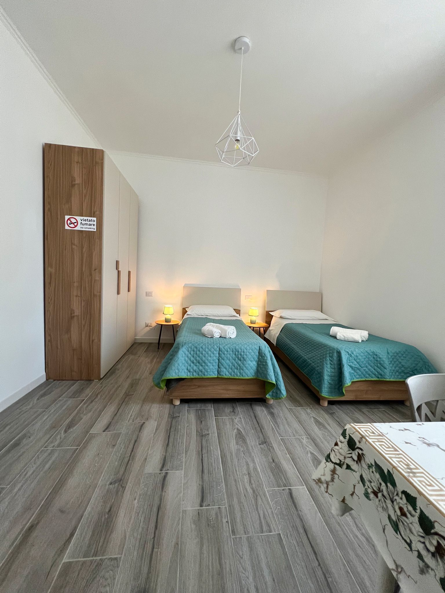 Ett hotellrum med två sängar, en garderob i trä, en skylt med texten ”rökning förbjuden” och en hängande lampa.