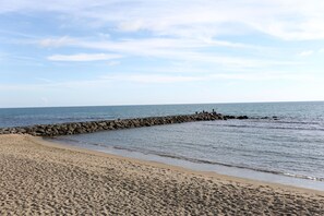Una playa arenosa con un rompeolas rocoso y mar tranquilo.