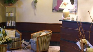 Vestíbulo de hotel con una recepción, dos sillones a rayas, una alfombra decorativa y un televisor montado en la pared.