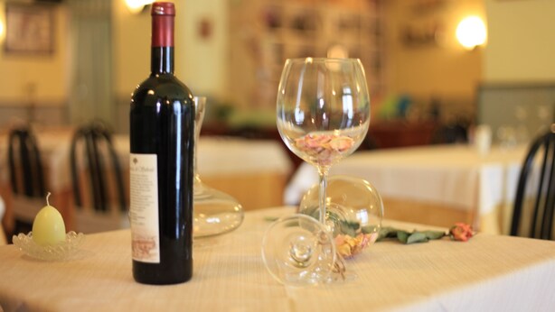 Una mesa con una botella de vino y dos copas, una vela y un arreglo floral.