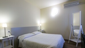 Habitación de hotel ordenada con cama, mesitas de noche, un espejo y un equipo de aire acondicionado.