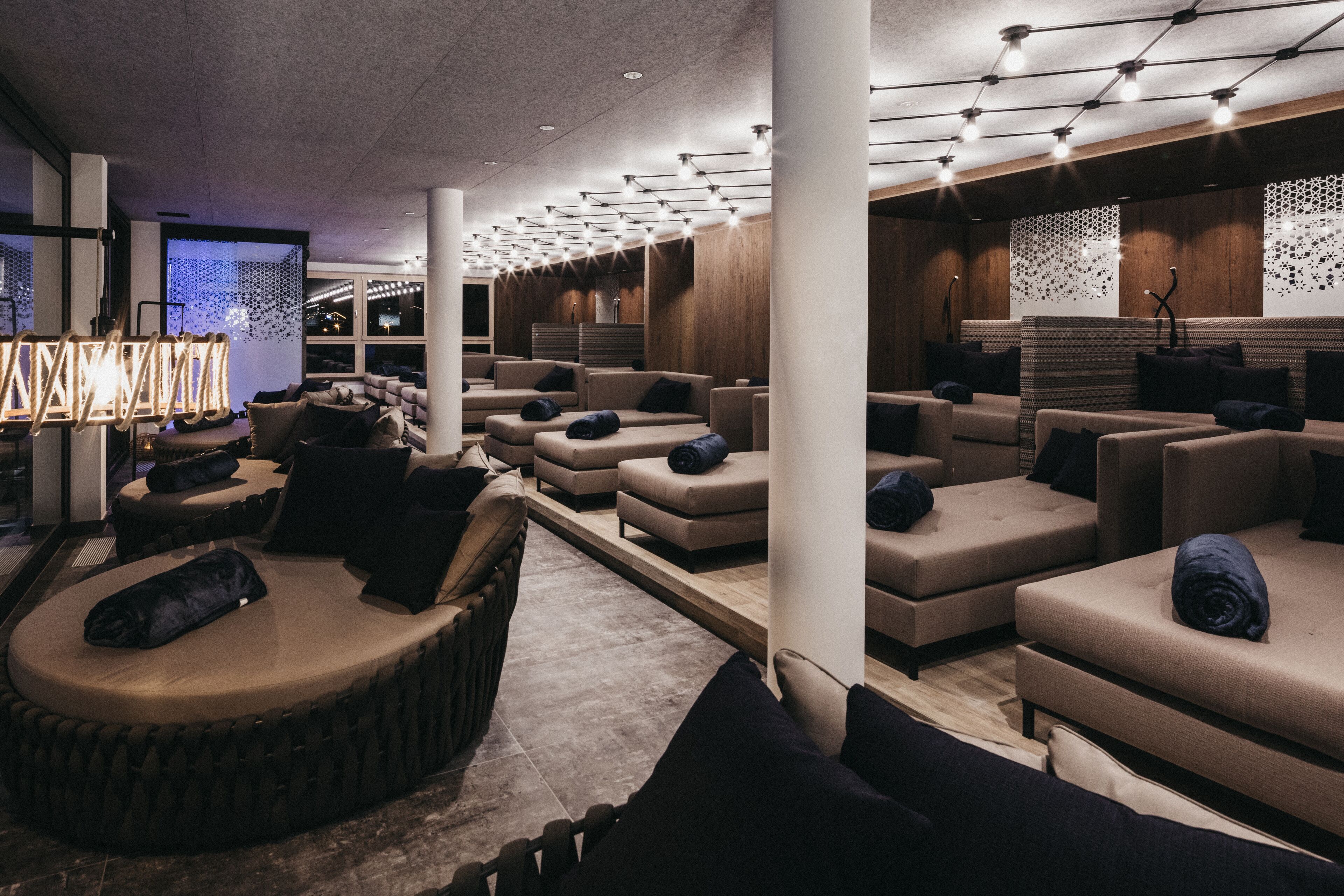 A modern lounge area with multiple seating options, including sofas and a circular seating area, with a decorative light fixture above.