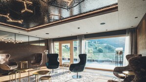 A modern living room with a large window, comfortable seating, and a unique ceiling design. - Hotel Tirolerhof (Tux)