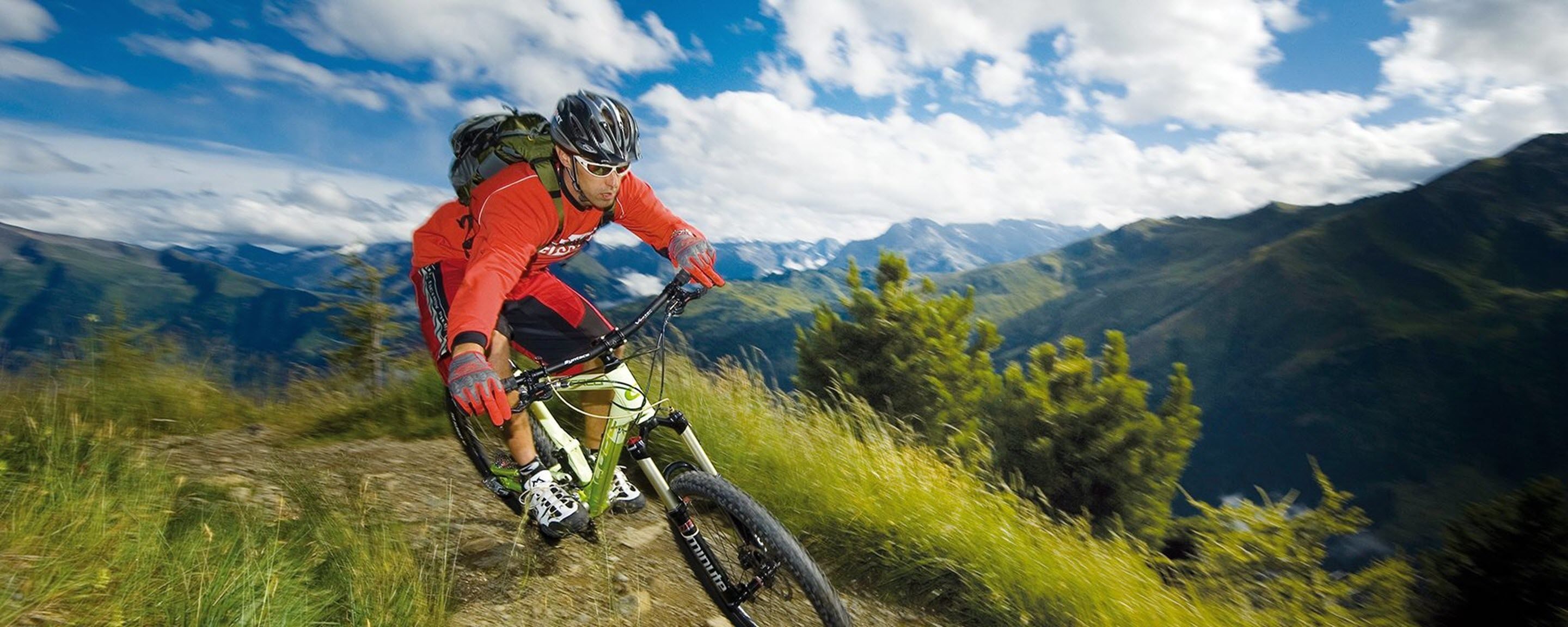 A mountain biker on a trail with a clear sky and distant mountains.