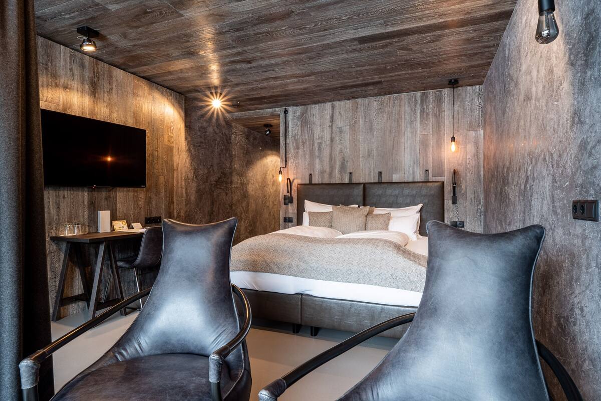 Un dormitorio moderno con una cama grande, dos sillones de cuero, un escritorio y un televisor de pantalla plana.