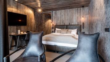 A modern bedroom with a large bed, two leather chairs, a desk, and a flat-screen TV.