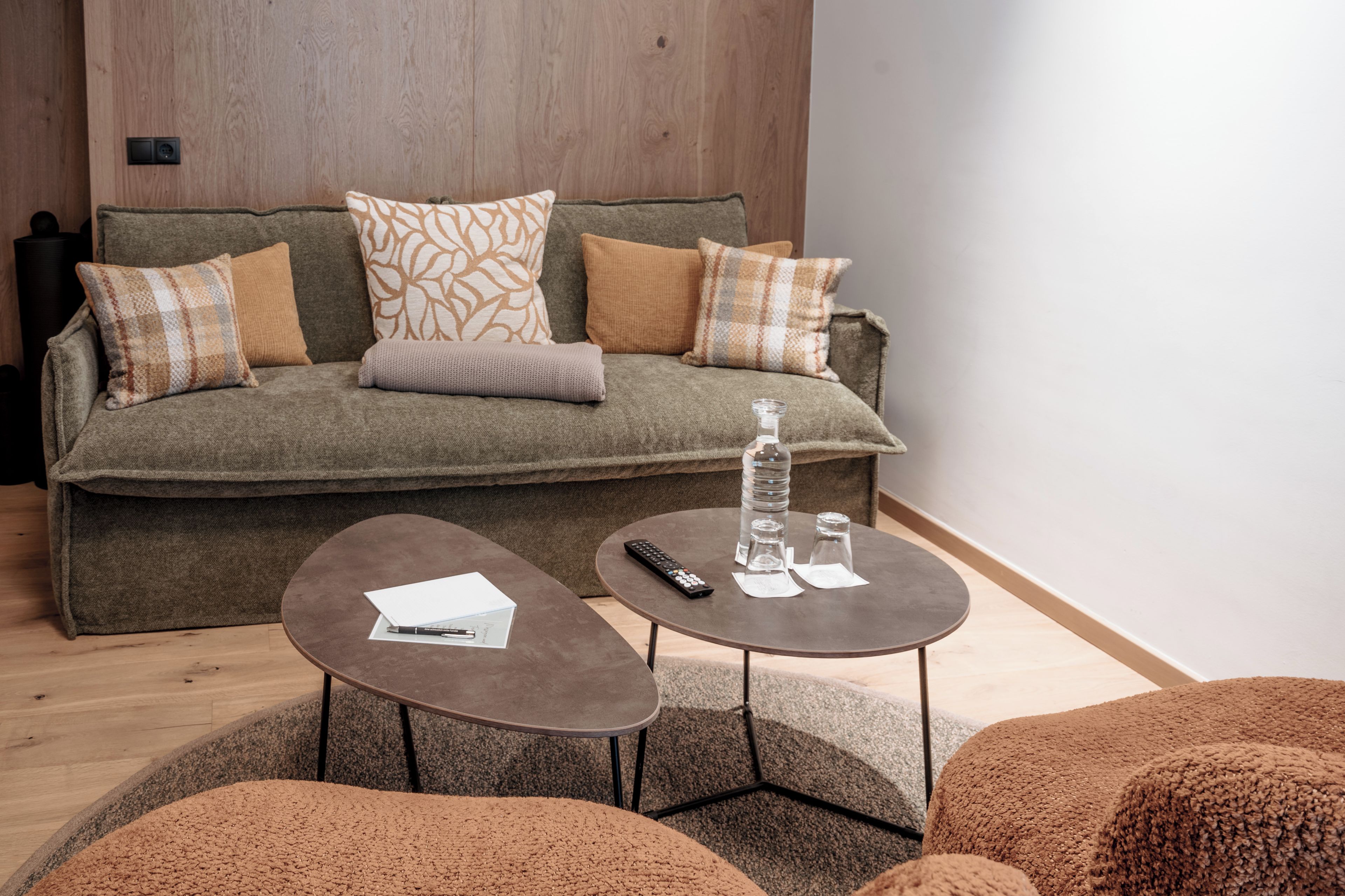 A modern living room with a sofa, two side tables, a remote control, and a water bottle.