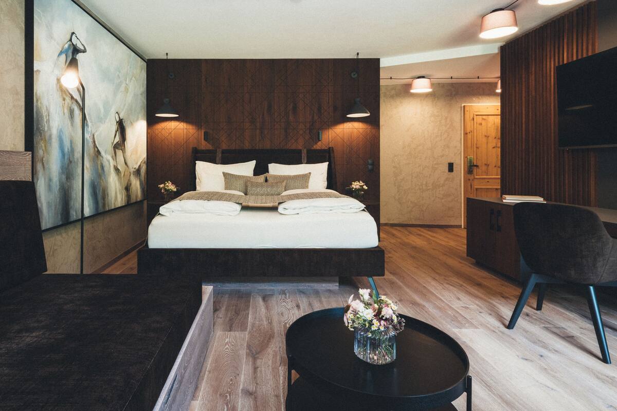 Un dormitorio moderno con una cama grande, una mesita de noche con un jarrón de flores, una silla y un cuadro en la pared.