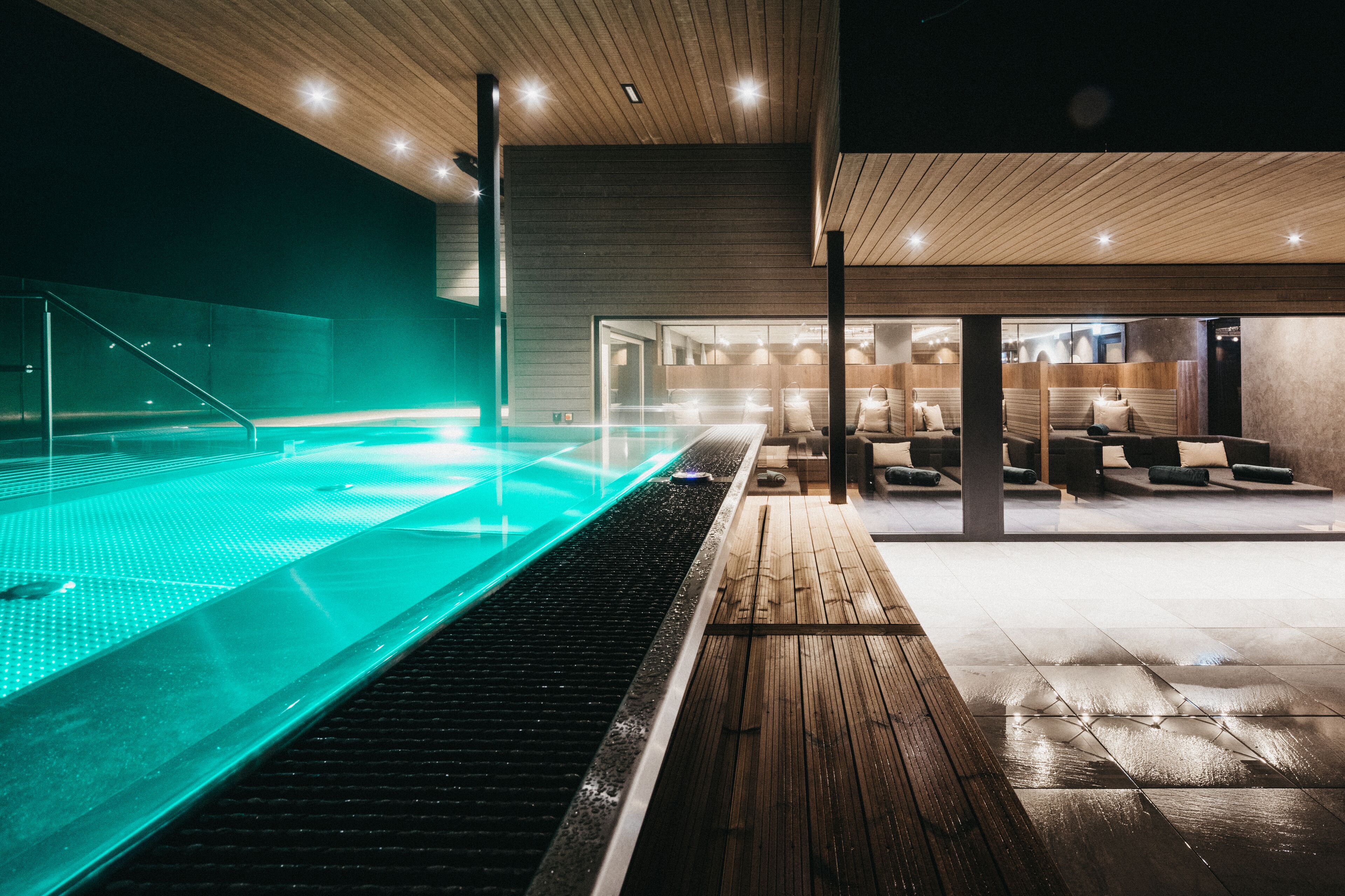 Una piscina interior moderna con una terraza de madera y zona de descanso.