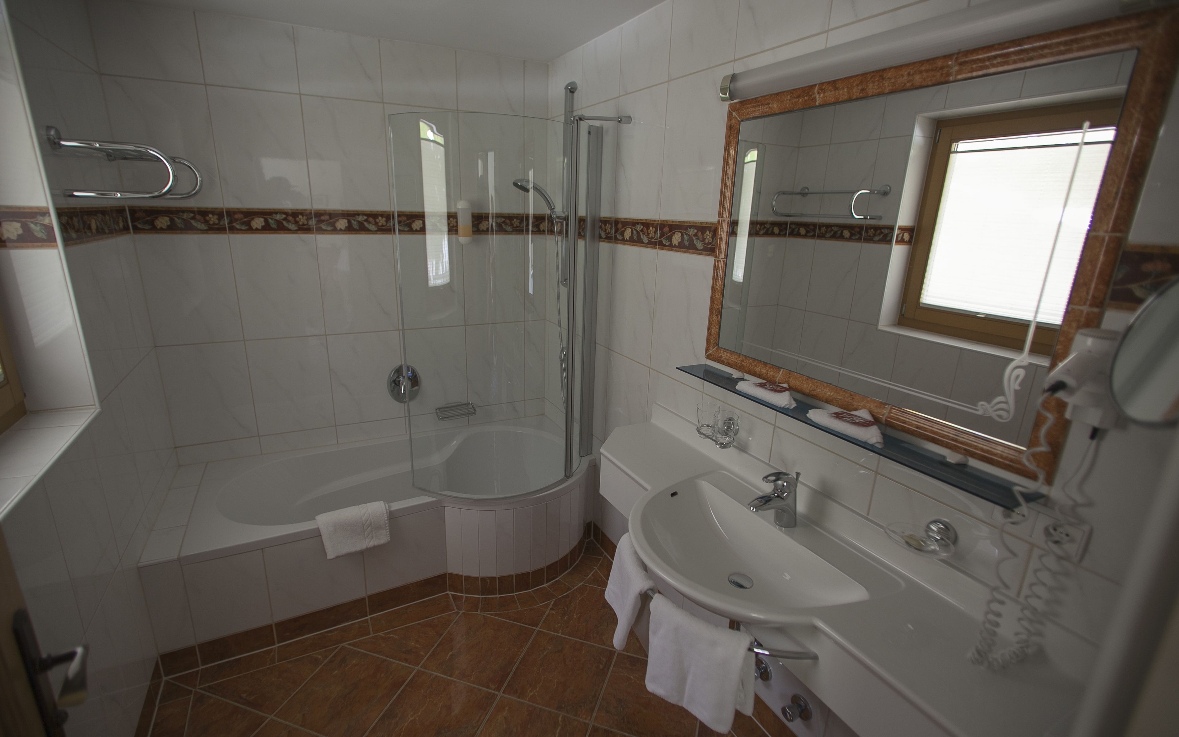 Un baño moderno con ducha envuelta en vidrio, bañera, lavamanos y tocador con espejo.