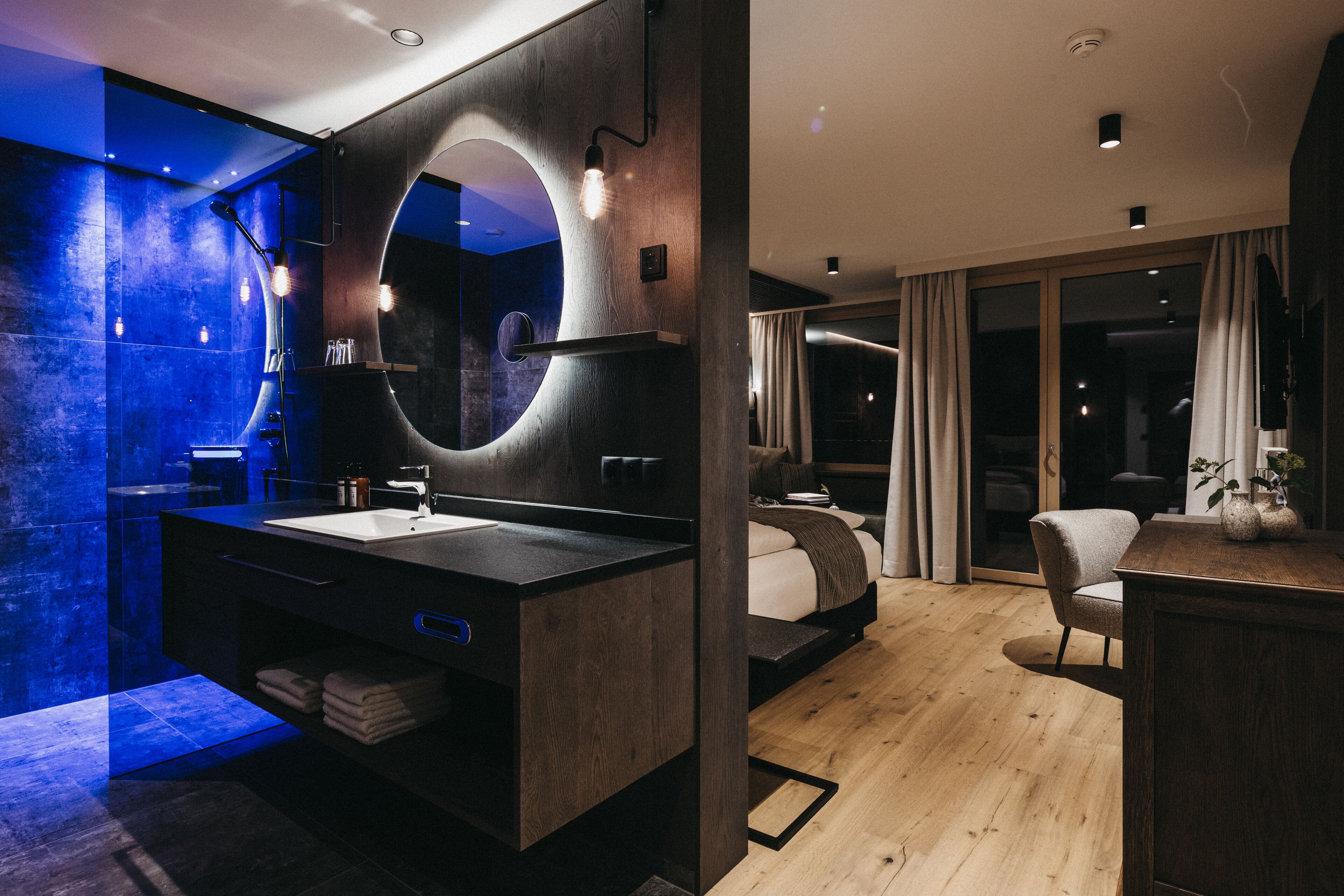 A modern bathroom with a large mirror, dark wood vanity, and a blue-lit shower area.