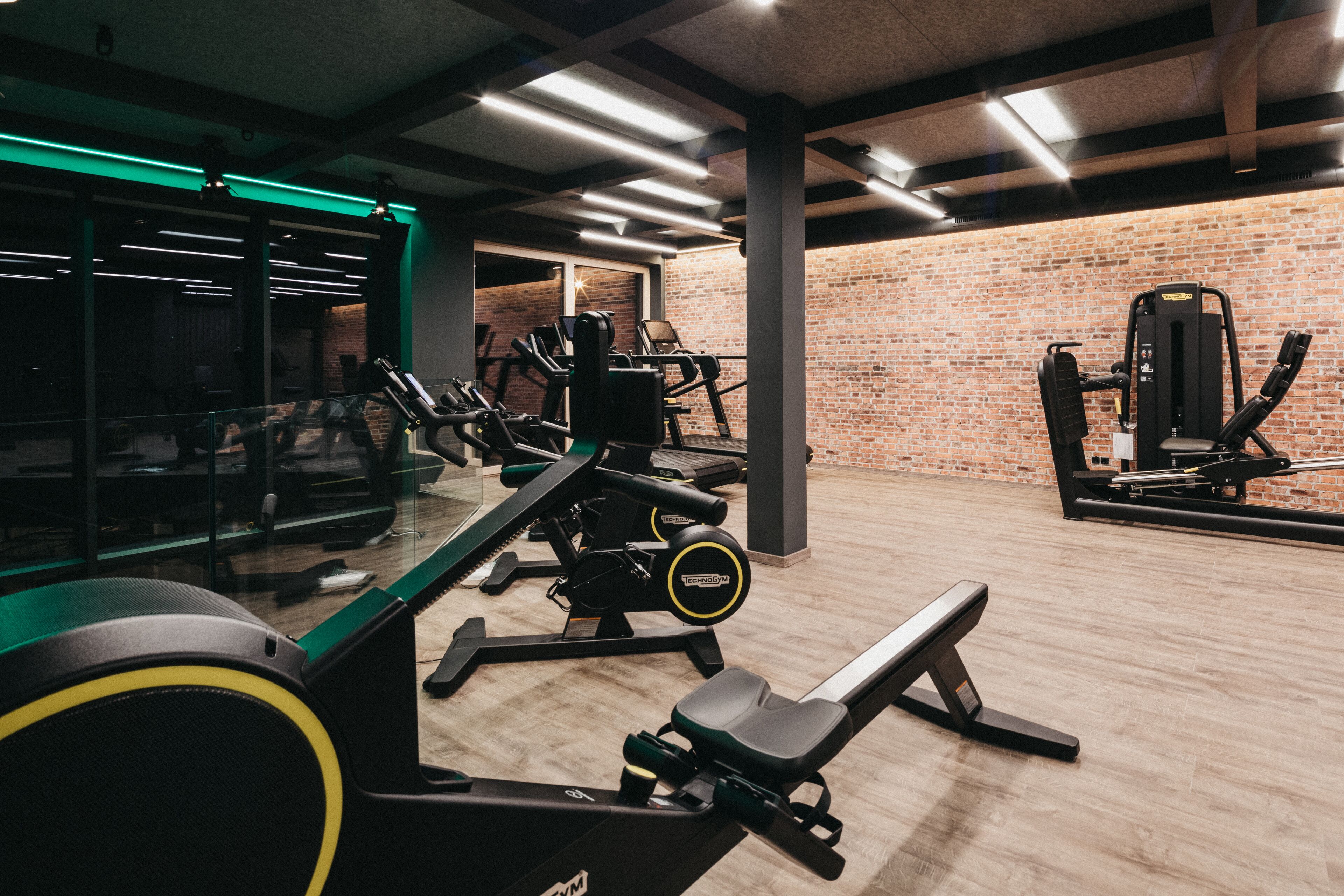 A gym with exercise equipment, a brick wall, and a wooden floor.