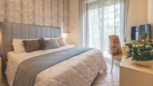 A bedroom with a large bed, a headboard, a bedside table, a television, and a window with curtains. - Hotel Athena (Cervia)
