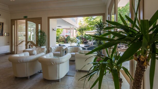 A spacious lobby with a seating area, large windows, and indoor plants. - Hotel Athena (Cervia)