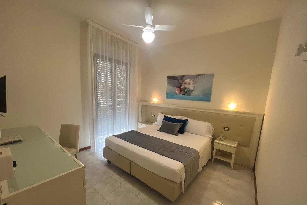 A hotel room with a bed, bedside tables, a desk, and a ceiling fan.