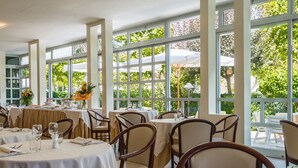 A restaurant with round tables and chairs, large windows, and outdoor umbrellas. - Hotel Athena (Cervia)