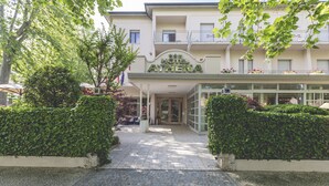 A hotel entrance with a paved pathway leading to the door, surrounded by greenery and a clear sky. - Hotel Athena (Cervia)