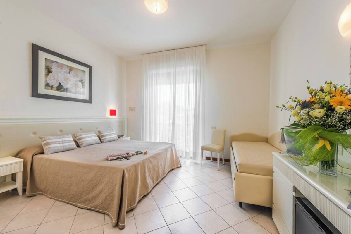 A hotel room with a bed, a chair, a desk, and a large window with curtains.