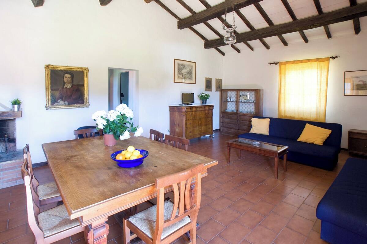 A dining area with a wooden table and chairs, a blue bowl with fruits, and a sofa with yellow cushions.