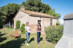 A stone building with a sloped roof, a wooden chair, and a bench in a grassy area. - Agriturismo Quercesecca - Nature & Relax  (Grosseto)