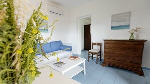 Een woonkamer met een witte bank, een houten dressoir, een witte salontafel en een schilderij aan de muur.