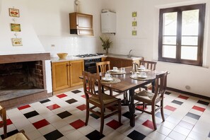 Una cocina con suelo de baldosas, armarios de madera, estufa, fregadero y una mesa de comedor con sillas.