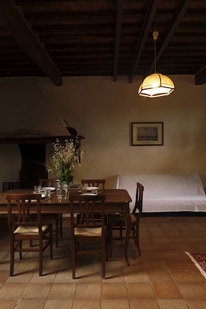 A dining area with a wooden table, chairs, a hanging light fixture, a framed picture on the wall, and a white sofa. - Agriturismo Quercesecca - Nature & Relax  (Grosseto)