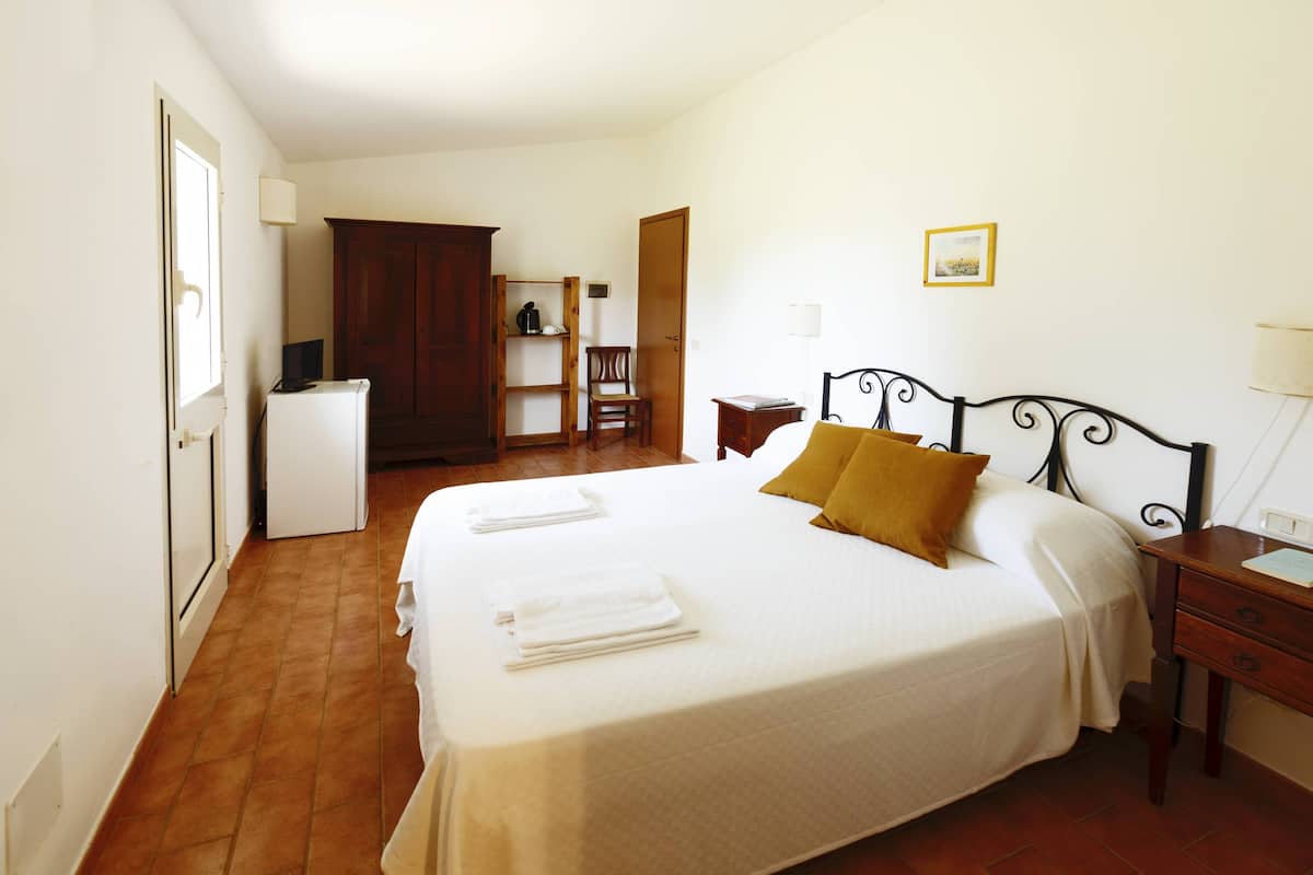 A hotel room with a bed, a desk, a chair, a wardrobe, and a small table with a lamp.