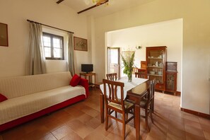 A living room with a sofa, dining table, chairs, a television, and a cabinet. - Agriturismo Quercesecca - Nature & Relax  (Grosseto)