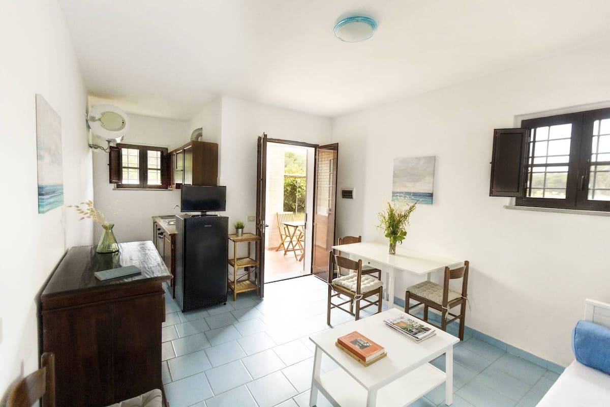 A compact kitchen with a refrigerator, a dining table with chairs, a small TV, and a door leading to an outdoor area.