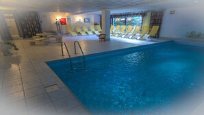 An indoor swimming pool with a tiled floor, a ladder, and yellow lounge chairs. - Hotel Garni Hubertus (Fulpmes)
