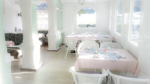 A room with white wicker furniture, a pink tablecloth, and a view through a window. - Hotel Garni Hubertus (Fulpmes)