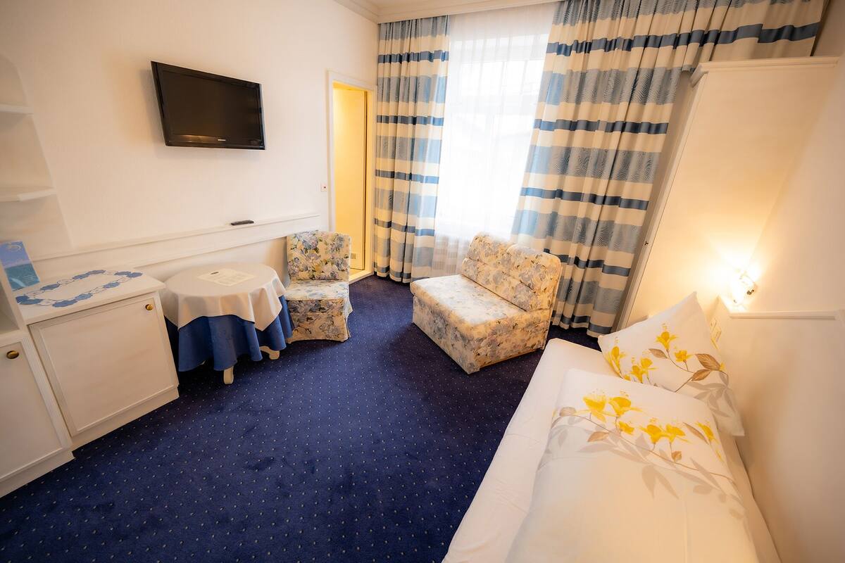 Une chambre d’hôtel avec un lit, une petite table, deux chaises, une télévision et des rideaux.