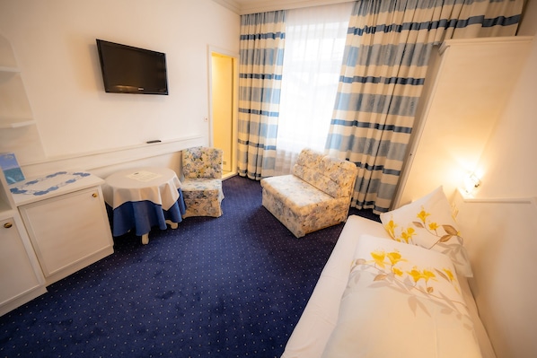 A hotel room with a bed, a small table, two chairs, a TV, and curtains.