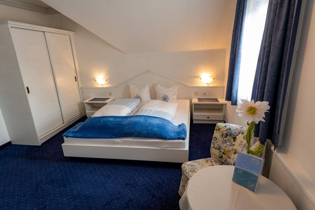 Une chambre d’hôtel comprenant un lit, des tables de chevet, un bureau, une chaise et un vase à fleurs.