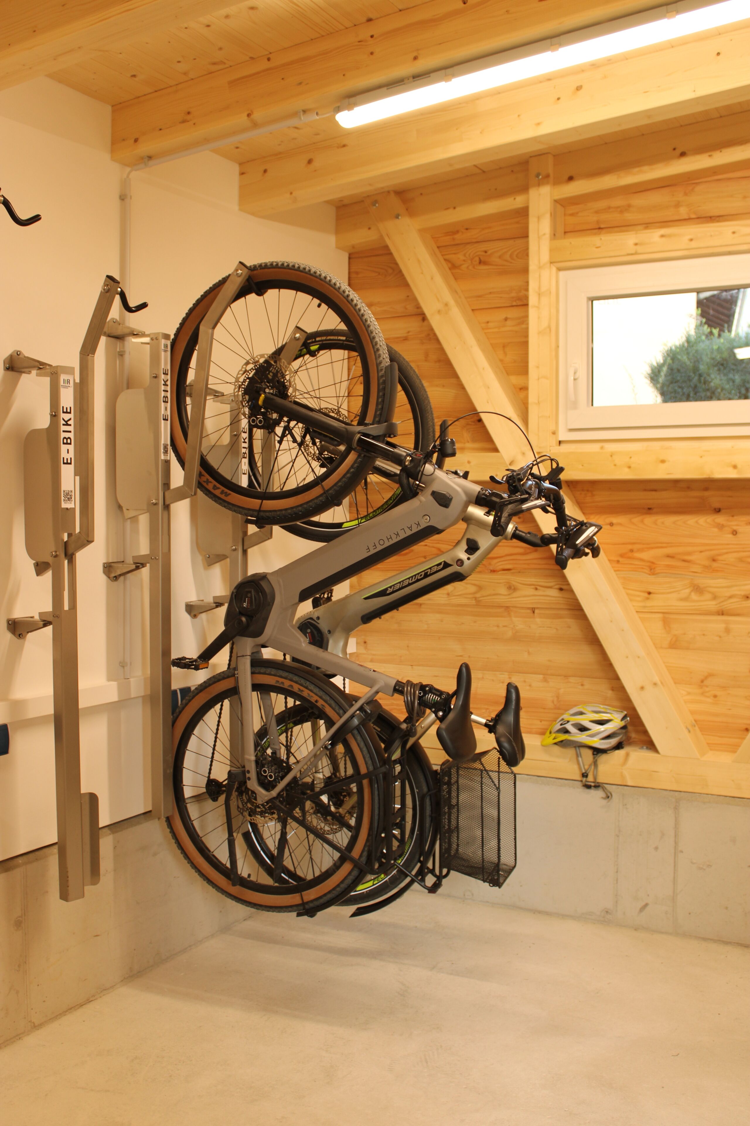 Una bicicleta colgada en un soporte de pared en una habitación con vigas de madera y un ventanal.